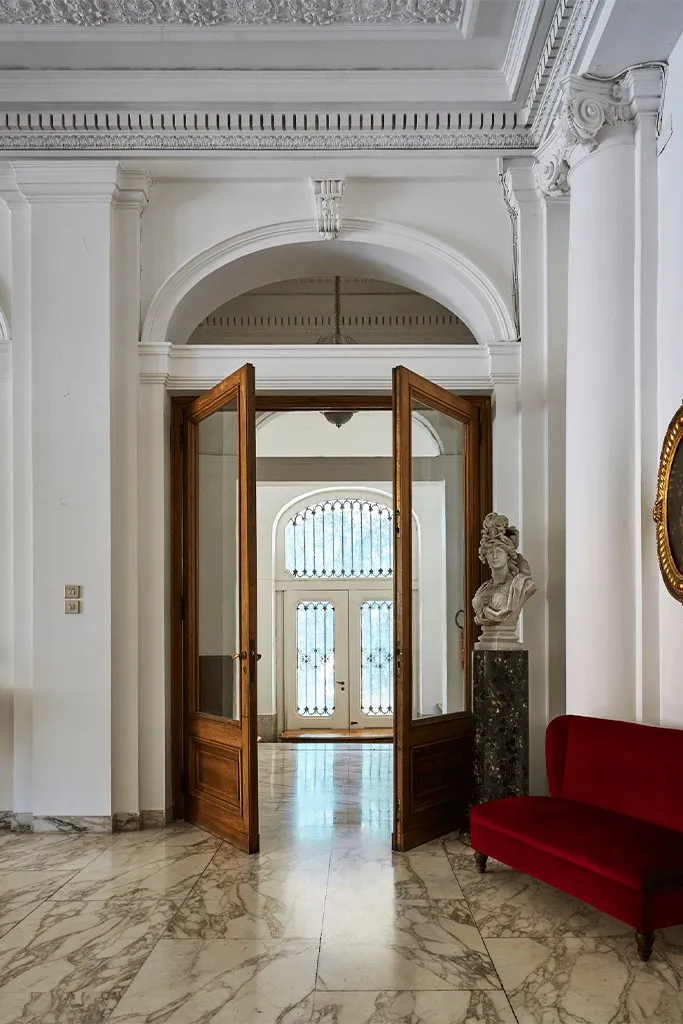 Ingresso del salone con porte in legno, busto e divanetto rosso